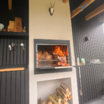 Braaimaster BI Single Black inbyggd i en öppen spis med brinnande eld